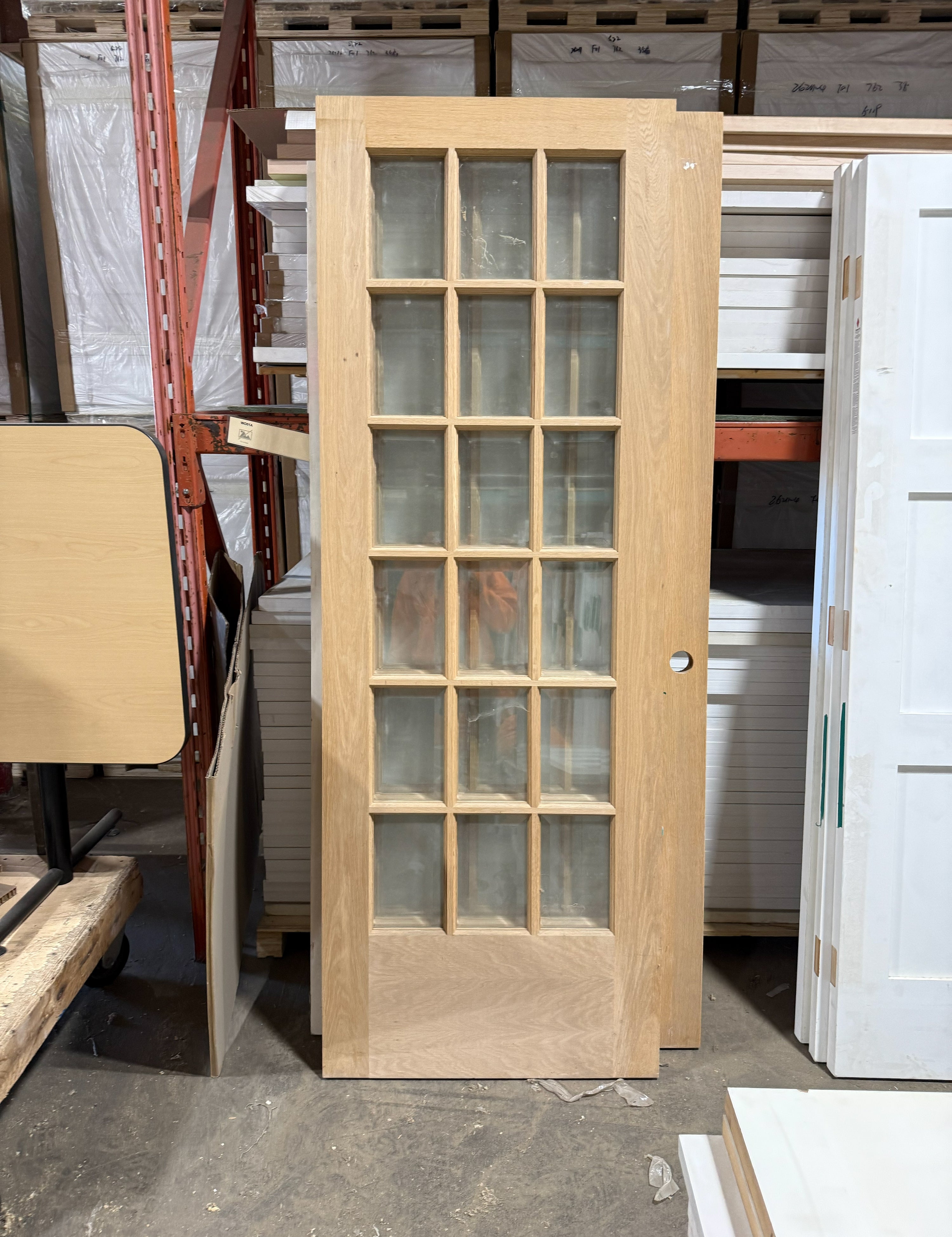 Unfinished white oak French door standing upright, clear glass panes three across above the solid wood panel at the bottom.