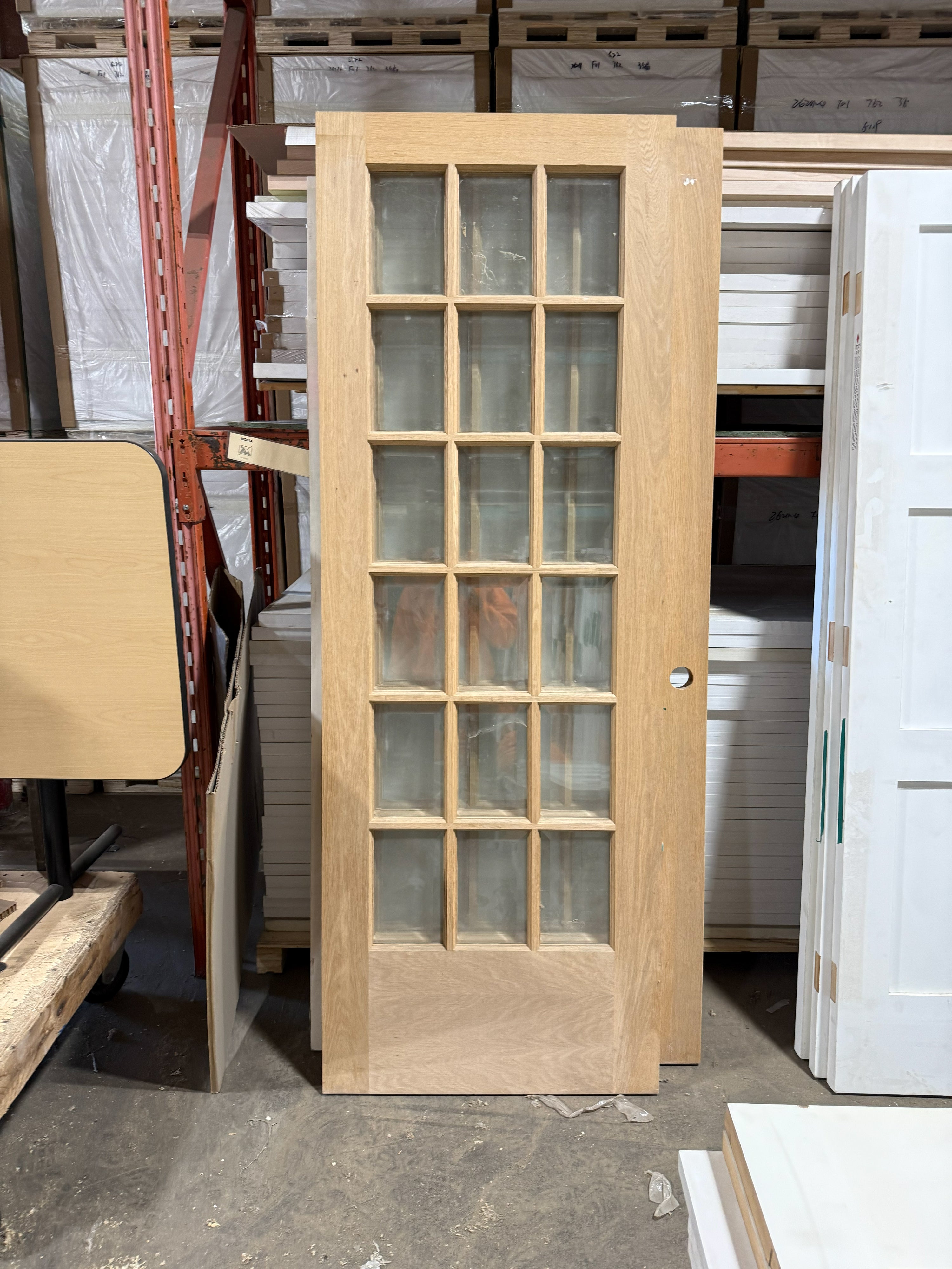 Unfinished white oak French door standing upright, clear glass panes three across above the solid wood panel at the bottom.