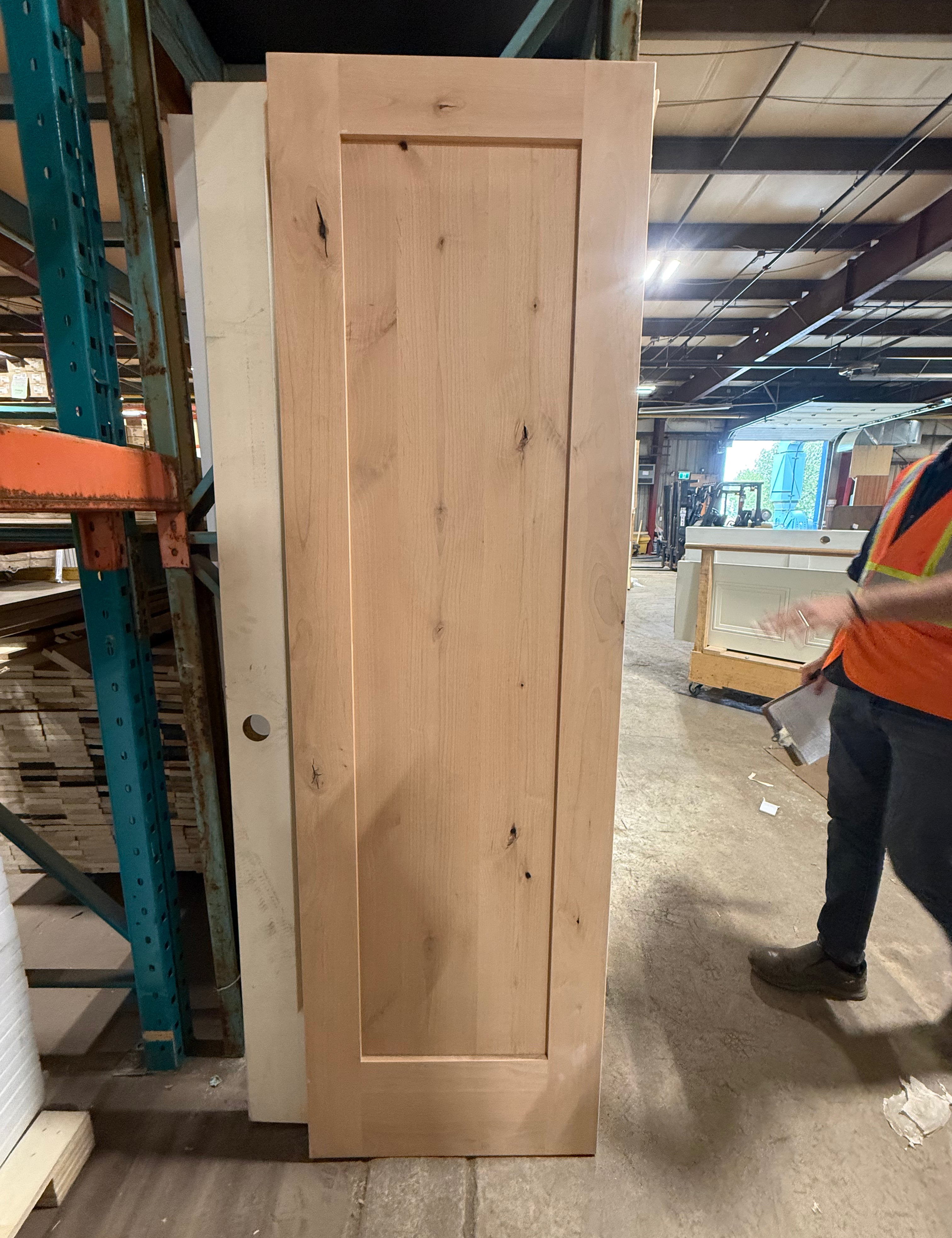 Knotty alder 1 panel Shaker door standing upright in the warehouse, blank with no handle hole cut into it, knots visible across the raw unfinished face.