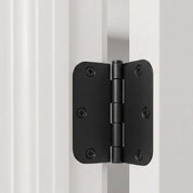 Matte black 3 inch door hinge with rounded corners on a white door