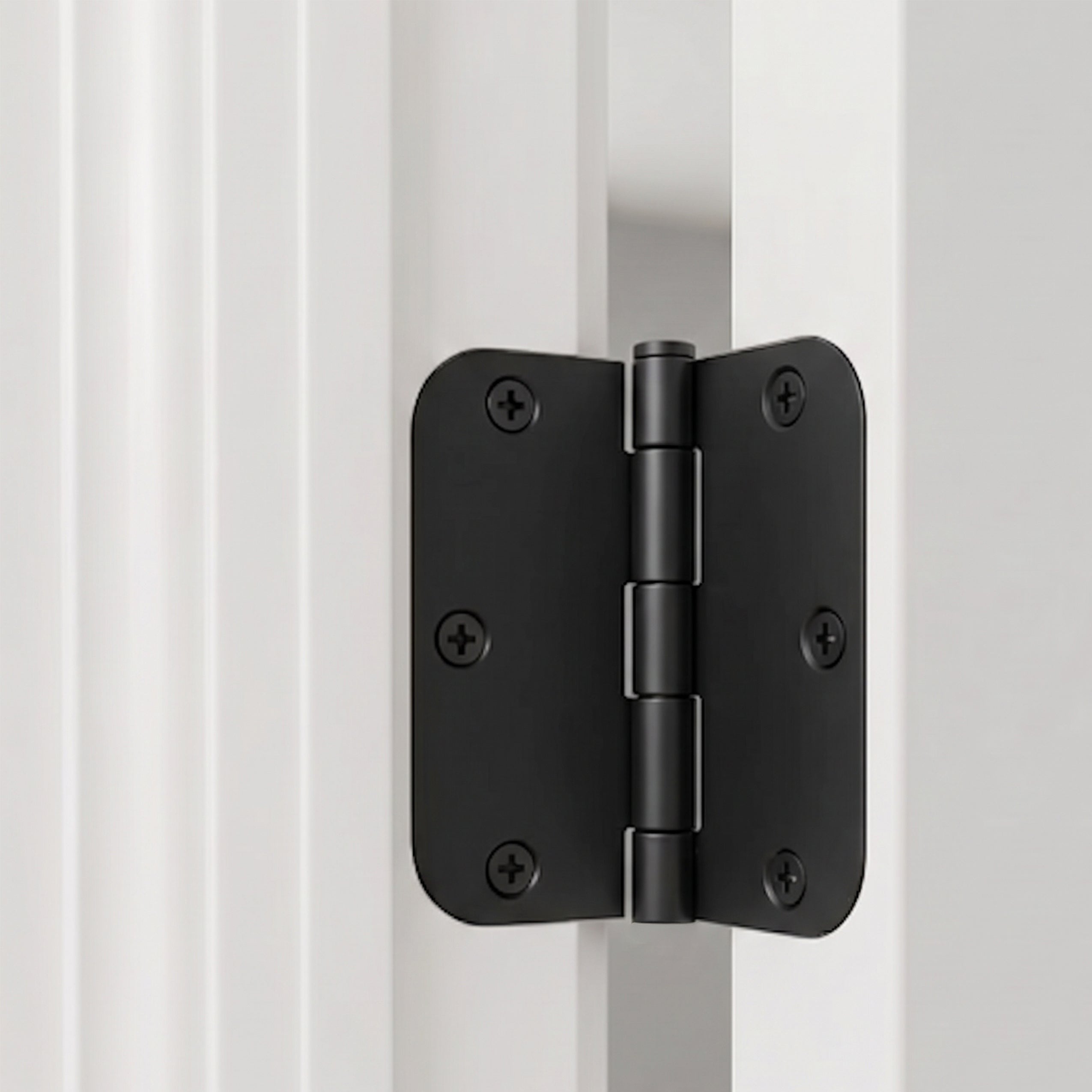 Matte black 3 inch door hinge with rounded corners on a white door